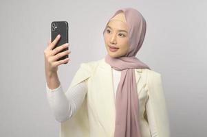 linda mulher muçulmana com hijab usando smartphone sobre fundo branco, conceito de tecnologia. foto