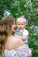 sincero retrato de jovem mãe sorridente com seu filho pequeno no jardim com flores lilás desabrochando. foto