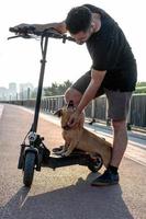 os pés de um homem de tênis fizeram parar uma perna com seu pequeno cachorro fofo na scooter elétrica nas ruas ou estacionar à luz do sol. foto