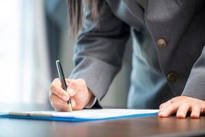 local de trabalho closeup pessoa profissional empresária sentada na mesa segurar caneta assinatura ou papel de contrato de assinatura. mulher funcionária escrevendo documento de acordo no formulário de papelada corporativa no escritório de trabalho foto