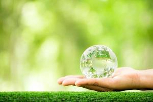 mão humana segurando o vidro do planeta globo na floresta verde com luzes da natureza bokeh. dia Mundial do Meio Ambiente. conceito de conservação do meio ambiente, proteger a terra de ecologia e a vida ambientalmente amigável. foto