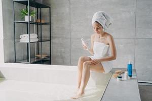 feminina massageando a perna usando cosméticos naturais para a pele anticelulite no banheiro. tratamento de cuidados com o corpo foto