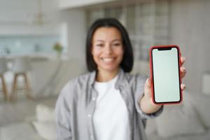 anúncio de aplicativos móveis. closeup feminino mostrando telefone com tela em branco simulada, de pé em casa foto