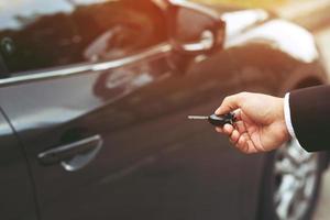 chave do carro na mão do homem de negócios. mão pressiona os sistemas de alarme de carro de controle remoto. trancar ou destrancar a porta. deixe espaço para escrever o texto. foto