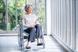 feliz mulher asiática idosa sentada na cadeira de rodas em casa, paciente de terapia sênior em casa conceito. foto