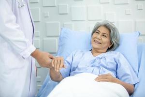 médico asiático apoiando e animando paciente sênior na cama na sala de recuperação. conceito de saúde e medicina. foto