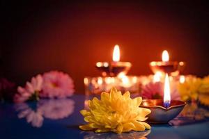 feliz Diwali. símbolos tradicionais do festival indiano de luz. queimando lâmpadas de óleo diya e flores sobre fundo vermelho. foto