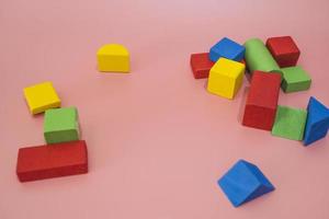 blocos de madeira coloridos em fundo rosa. brinquedos de criatividade. blocos de construção infantil. formas geométricas - cubo, prisma triangular, cilindro. o conceito de pensamento lógico. foto