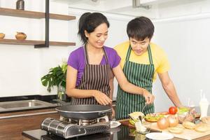 família feliz. casal adorável asiático, mulher bonita e homem bonito está preparando ingredientes e cozinhando comida para tomar café da manhã na cozinha foto