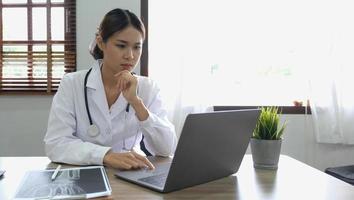 médico de mulher asiática feliz retrato, conceito de telemedicina. médica asiática falando com paciente usando consulta de webinar de vídeo on-line de laptop enquanto está sentado no escritório da clínica foto