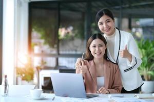 duas jovem e bela mulher de negócios asiáticos na conversa, trocando ideias no computador portátil juntos no escritório. foto