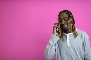 cara afro usa um telefone enquanto posava na frente de um fundo rosa. foto