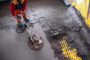 trabalhador realizando e polindo piso de betonilha de areia e cimento foto