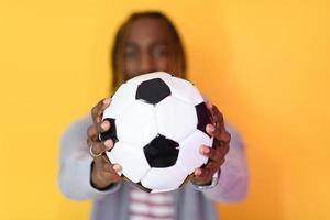 homem afro posando em um fundo amarelo enquanto segura uma bola de futebol foto