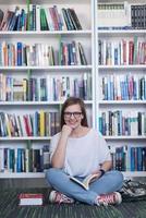 Famale estudante lendo livro na biblioteca foto