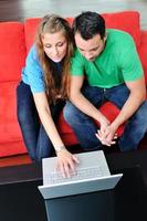 casal feliz se diverte e trabalha no laptop em casa foto