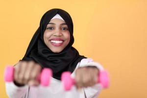 mulher afro muçulmana promove uma vida saudável, segurando halteres nas mãos foto