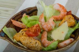 salada caesar com camarões em uma tigela sobre fundo de madeira foto