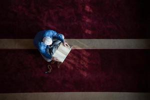 homem muçulmano rezando sozinho a Deus dentro da mesquita e lendo o livro islâmico de azevinho foto