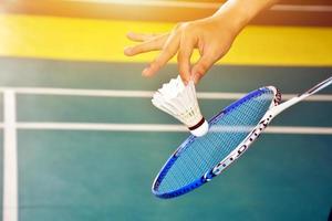 jogador de badminton segura raquete e peteca de creme branco na frente da rede antes de servir para o outro lado da quadra. foto