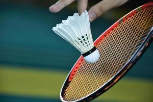 jogador de badminton segura raquete e peteca de creme branco na frente da rede antes de servir para o outro lado da quadra. foto