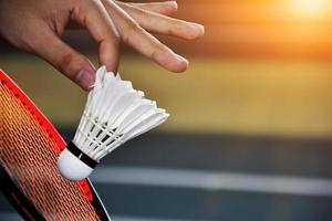 jogador de badminton segura raquete e peteca de creme branco na frente da rede antes de servir para o outro lado da quadra. foto