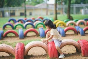 sorriso de linda garota asiática brinca pulando na escola ou jardim de infância ou playground. atividade de verão saudável para crianças. menina asiática escalando ao ar livre no playground. criança brincando no playground. foto