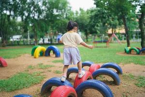 sorriso de linda garota asiática brinca na escola ou jardim de infância ou playground. atividade de verão saudável para crianças. menina asiática escalando ao ar livre no playground. criança brincando no playground ao ar livre. foto