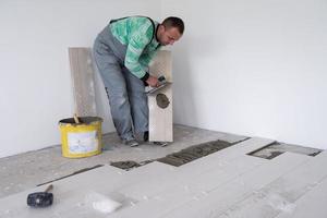trabalhador instalando as telhas cerâmicas de efeito de madeira no chão foto
