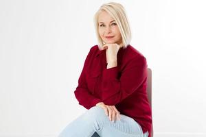 fechar o retrato de uma mulher loira sorridente na camisa vermelha elegante, sentada na cadeira no fundo branco foto