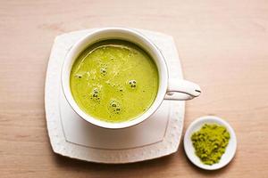 chá verde matcha japonês é derramado em uma caneca branca e em um pires branco em pó. conjunto de chá em um guardanapo texturizado. bebida revigorante em um café, culinária, alegria, antioxidante. espaço para texto foto