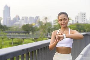 uma jovem fitness em roupas esportivas usando relógio inteligente enquanto se exercita no parque da cidade, saudável e estilos de vida. foto