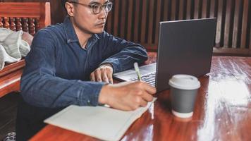 homem de negócios teleconferência do homem de negócios em casa em reunião usando seu computador portátil e escrevendo notas foto