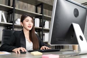 retrato de mulher de negócios bonita usando computador no local de trabalho em um escritório. senhora de negócios positiva sorrindo olhando para a tela do computador. foto