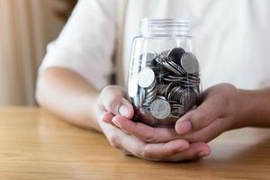 mãos adultas segurando uma jarra com moedas no conceito de poupança e doação foto