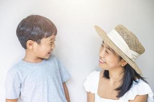 retrato bela viajante mãe asiática de vestido branco, chapéu de palha e filho de camisa cinza gosta de relaxar sorriso lazer no resort em férias de praia tropical foto