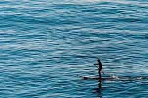 um homem remando de pé sobre uma mesa de surf no mar azul profundo foto