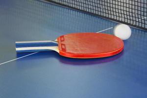 raquete vermelha, bola de tênis na mesa de ping pong azul foto