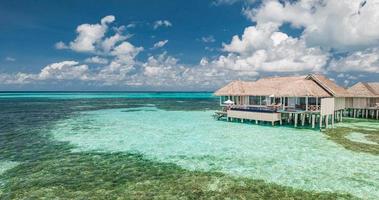 vista aérea da ilha das maldivas, resort de villas de água de luxo e cais de madeira. lindo céu e fundo de praia da lagoa do oceano. férias de férias de verão e conceito de viagens. paraíso paisagem aérea pano