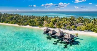 vista aérea da ilha das maldivas, resort de villas de água de luxo e cais de madeira. lindo céu e fundo de praia da lagoa do oceano. conceito de viagens de férias de férias de verão. panorama de paisagem aérea do paraíso
