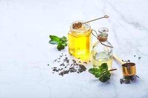 garrafa de óleo essencial de hortelã e folhas verdes e pote de mel. ingredientes orgânicos naturais para cosméticos, cuidados com a pele, cuidados com o corpo. conceito de cuidados de beleza foto