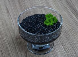 caviar preto em uma tigela sobre fundo de madeira foto