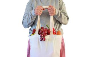 mulher segura sacola de compras reutilizável verde ecologicamente correta cheia de produtos de mercearia frescos completos de frutas e legumes isolados no fundo branco com traçado de recorte foto