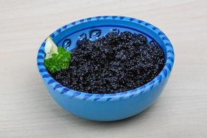 caviar preto em uma tigela sobre fundo de madeira foto