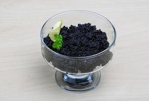 caviar preto em uma tigela sobre fundo de madeira foto