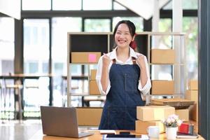 startup pequena empresa empreendedora sme ou mulher asiática freelance usando um laptop com caixa, jovem mulher asiática de sucesso com a mão levantada, caixa de embalagem de marketing on-line e entrega, conceito sme. foto