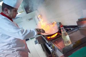 chef na cozinha do hotel preparar comida com fogo foto