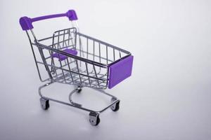 mini carrinho de compras vazio decorativo com elementos violetas em fundo branco, com espaço de cópia. foto