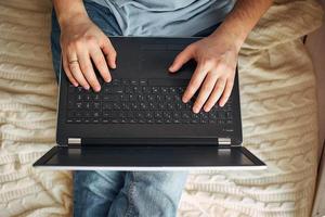 vista superior das mãos masculinas usando o laptop moderno, close-up do jovem trabalhando em casa e usando o notebook, a mão do homem usando tecnologia foto