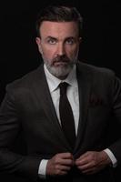 retrato de um elegante elegante empresário sênior com barba e roupas de negócios casuais em estúdio fotográfico ajustando terno foto